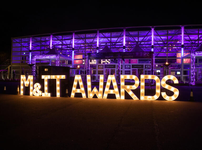 An M&IT Awards sign outside a conference venue lit up at night.