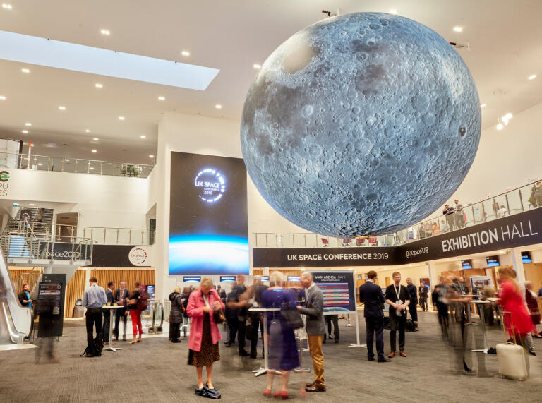 Delegates in an exhibition centre with a large moon hanging from the ceiling.