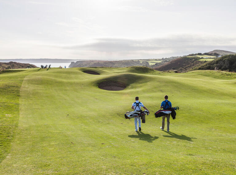 Golfers walking to the next tee with views of the coastline at Pennard Golf Club.