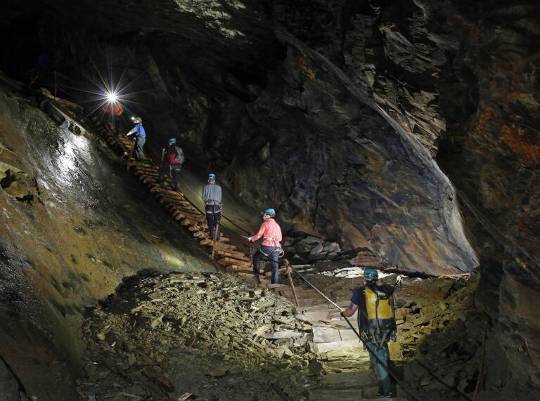 Group of people wearing safety gear climbing up steps in an underground cave.