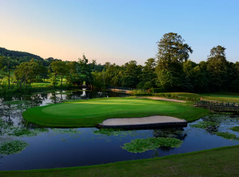 Sunset over a lake and golf course surrounded by trees.