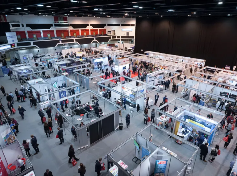 Exhibition space with shell scheme stands and people walking around.