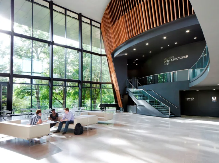 People on settees in a foyer adorned with dark wood and large windows.