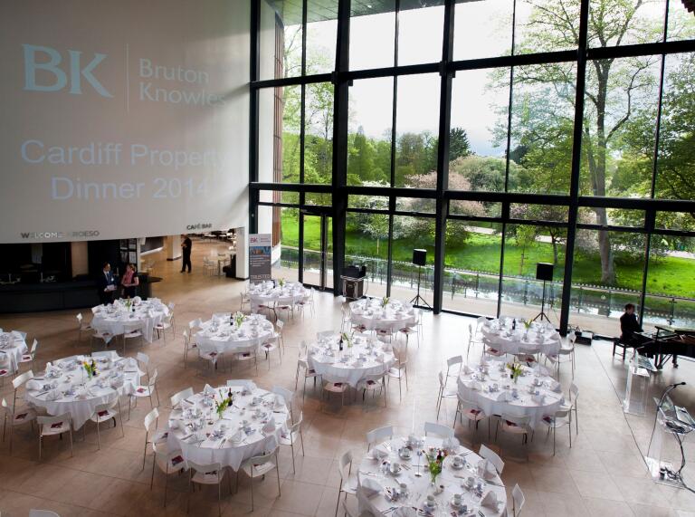 Hall set up with round dining tables, looking onto green parkland with floor to ceiling windows.