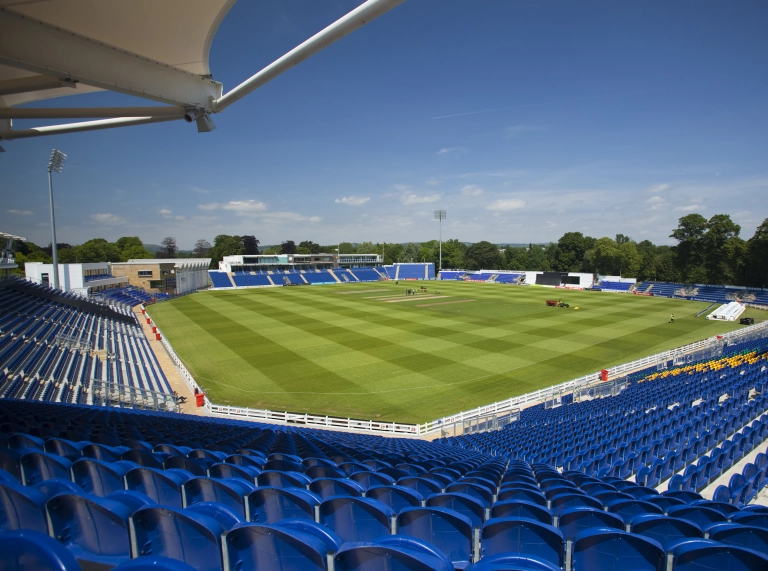 View of a cricket pitch from seats inside a stadium.