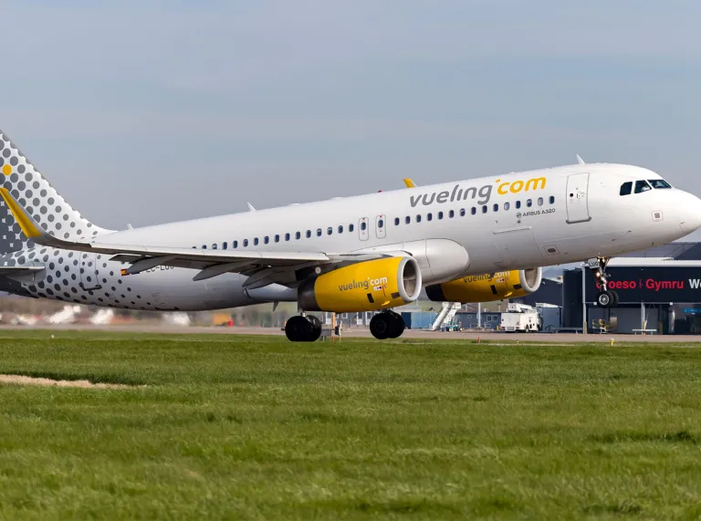 Plane on runway with yellow jet and branding and Welcome to Wales sign in black and red on Airport .
