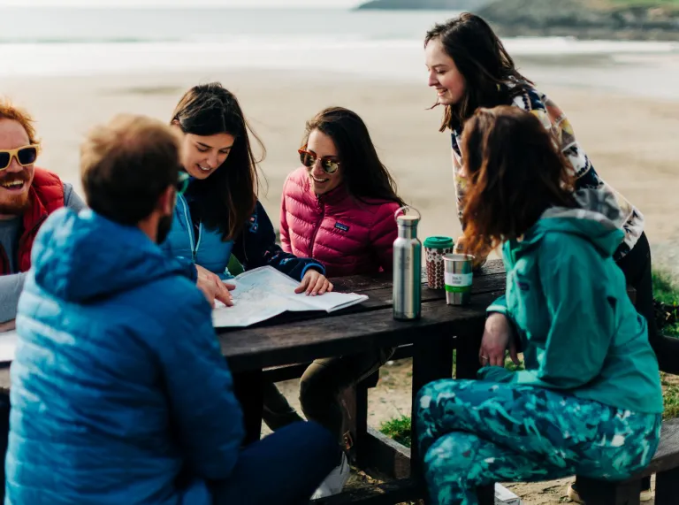 A group of people sitting on a park bench by the sea looking at a map.