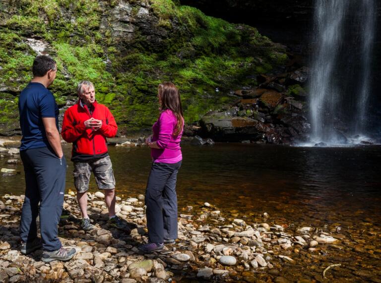 3 people standing in front of a waterfall talking.