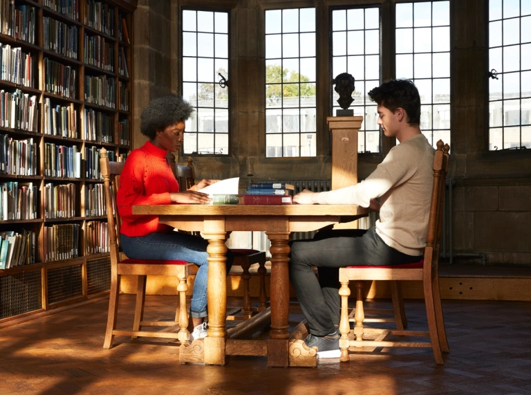 Two students in a university library sitting at a desk