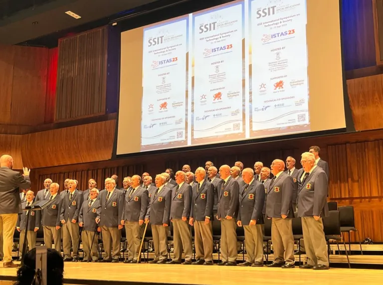 male voice choir on stage in suits with the conference banner behind them