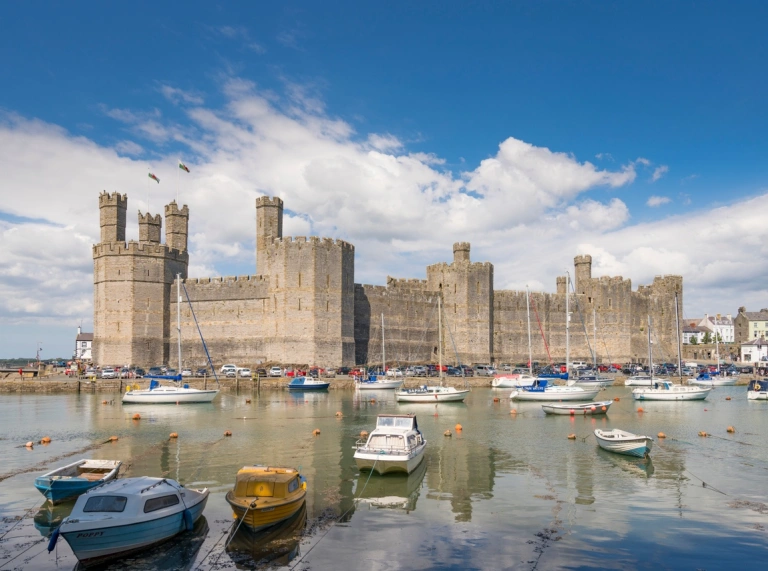 exterior shot of Caernarfon Castle set against teh harbour with small boats on