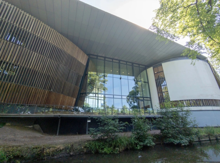 Outside of building with blue water and trees against the glass foyer entrance