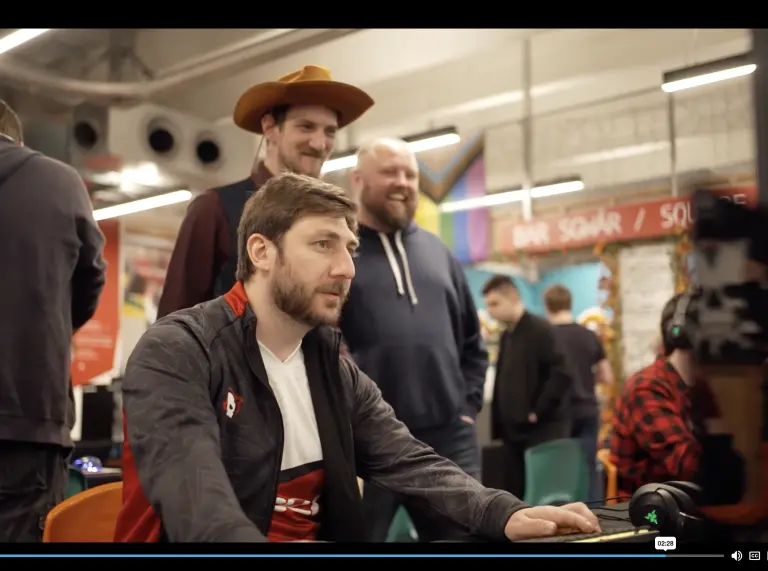 John Jackson sitting at the computer with two people standing behind laughing one wearing a cowboy hat