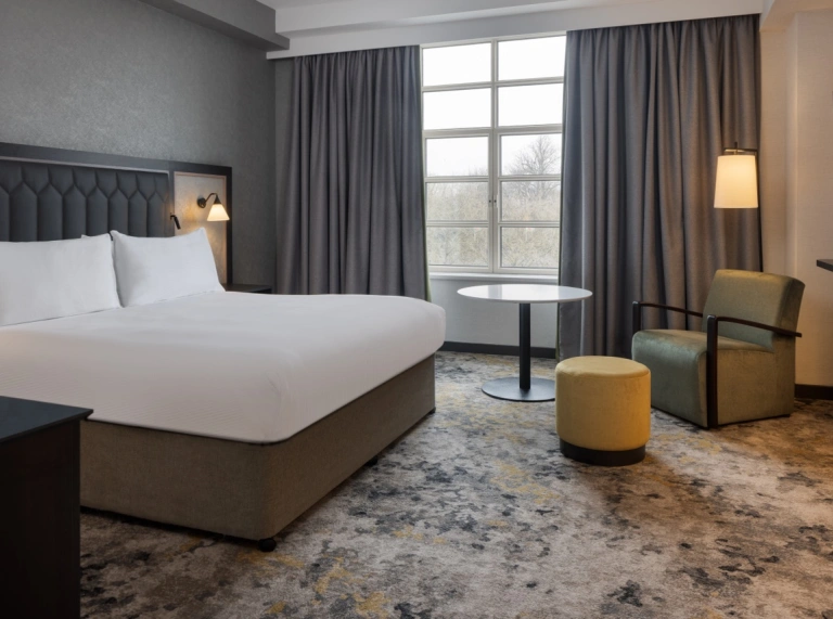 Hilton Cardiff bedroom with light patterned carpet with large window and view of trees and large bed with white sheets