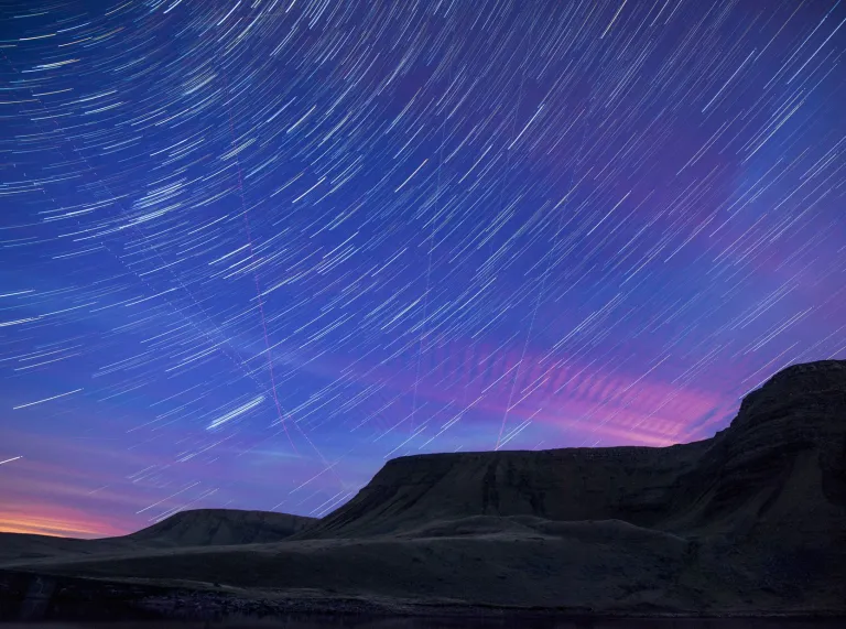 Dark Sky image of black mountain and blue purple night sky wuth shooting stars