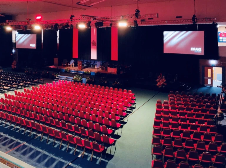 USW sports hall at Treforest set out with stage and red chairs facing teh stage and large screens 