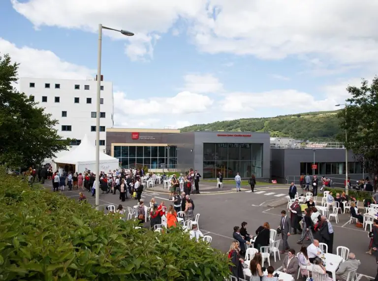 image of foyer exterior of the Trefirest campus with peopole on plastic seats and standing talking