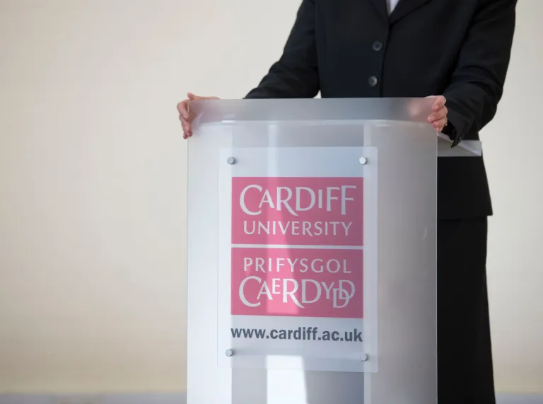 lecturers hands resting on podium wuth Cardiff University bilingual branding 