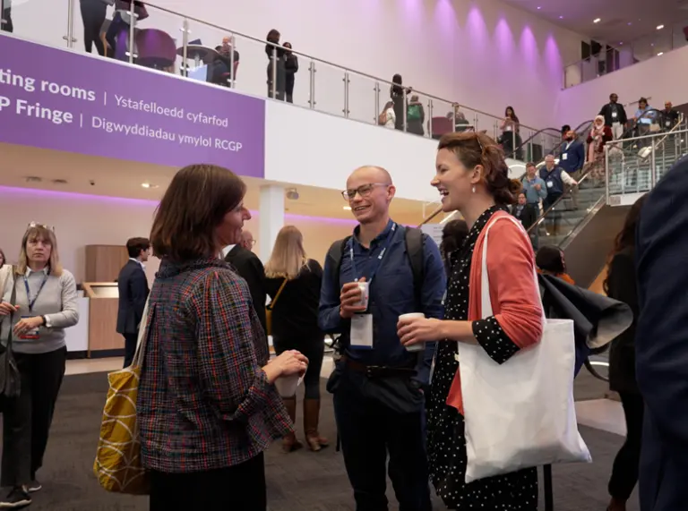 A busy conference lobby with delegates talking in small groups, with signage for meeting rooms and the RCGP Fringe visible on the upper level