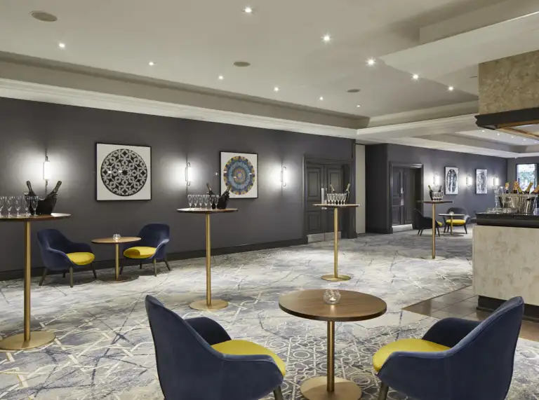 A stylish pre-function lounge with contemporary artwork, soft seating in navy and yellow tones, and tall cocktail tables set for drinks