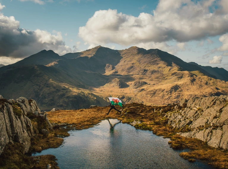 Person holding a Welsh flag overlooking Snowdonia mountain landscape