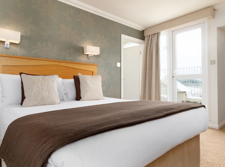 Double bedroom with wooden headboard, neutral décor, wall lights, and a window with balcony view. 