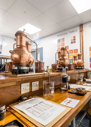 Distillery bottles and vats on a desk in a botanical room.