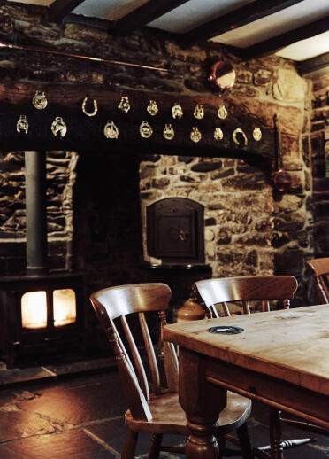 Table and chairs in front of a log fire built into a stone wall.