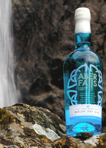 A blue bottle of Aber Falls welsh dry gin set against a waterfall.