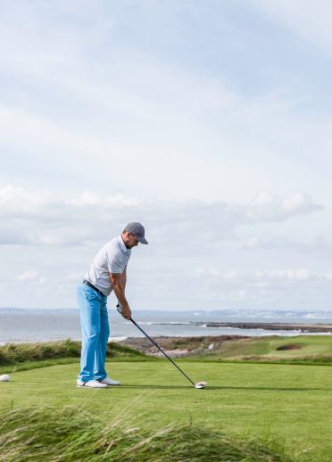 Golfer about to tee off with views of the coastline.