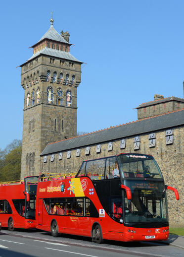 Open top sightseeing bus outside a castle and clock tower.