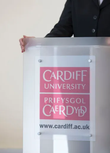 lecturers hands resting on podium wuth Cardiff University bilingual branding 