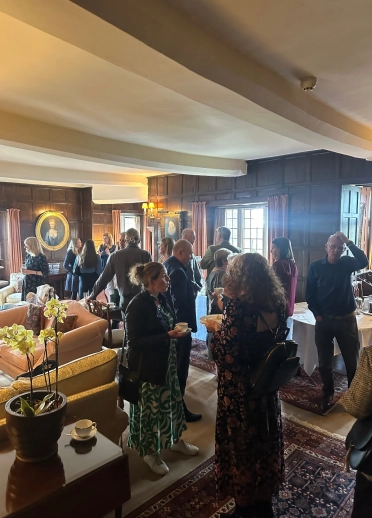 A group of people networking in an elegant wood‑panelled lounge with sofas, rugs, and large windows.