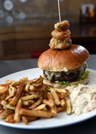 A burger topped with a stack of onion rings, chips and relish.