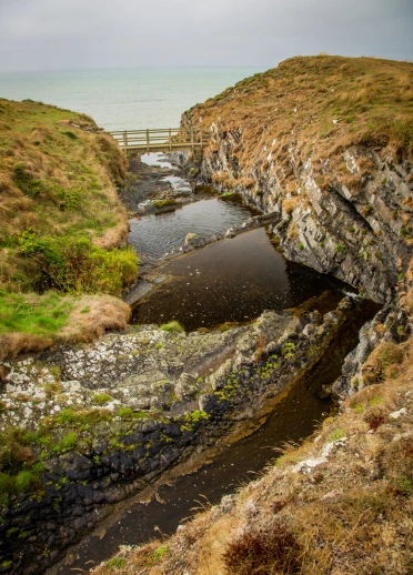 Rugged rocks and coves of the Wales coast connected by a foot bridge.