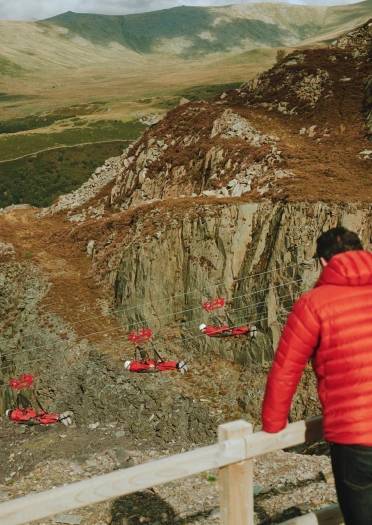 A man on a viewing platform looking down at adventurers zip lining down an old quarry.