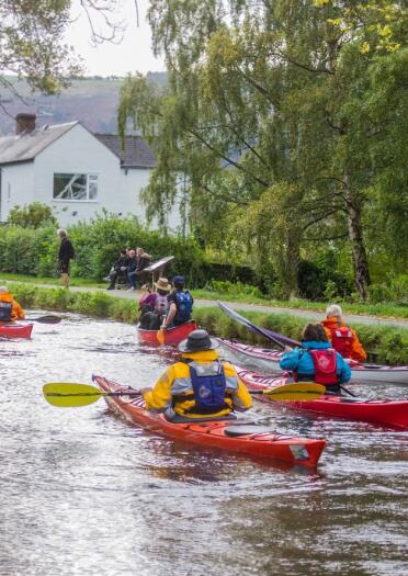 A group of people canoeing down a river in colourful protective waterproofs.