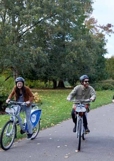 Three people on bicycles, cycling through a park.