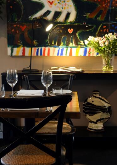 A dining table laid with wine glasses and a large colourful artwork on a feature wall.