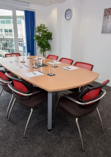A boardtoom table and chairs with water, glasses, pens and paper.