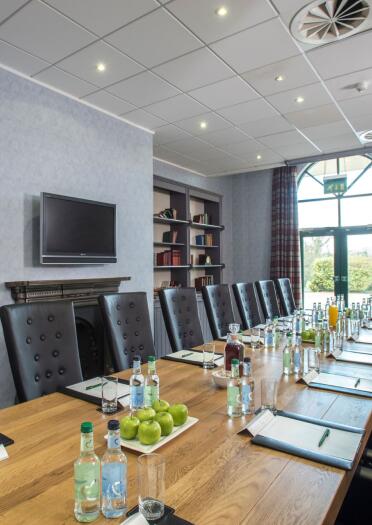 A long boardroom table and chairs with fruit, water and stationery.