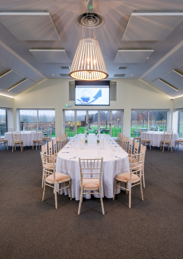 A conference room in a glass fronted building with an oval table, chairs and screen.