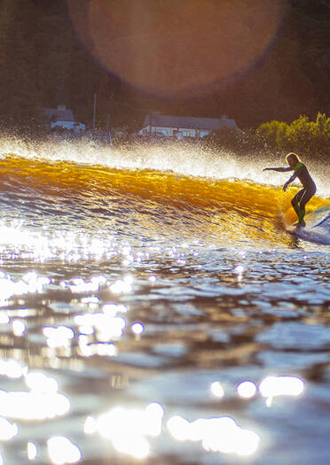 Surfer on an inland surf lagoon, with sun shining on the water.