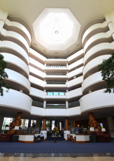 A large atrium in a hotel with a glass sunlit roof and trees.