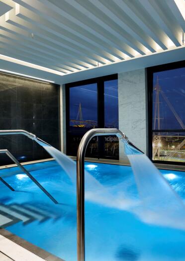 A spa pool with spraying fountains against large glass windows in a hotel.