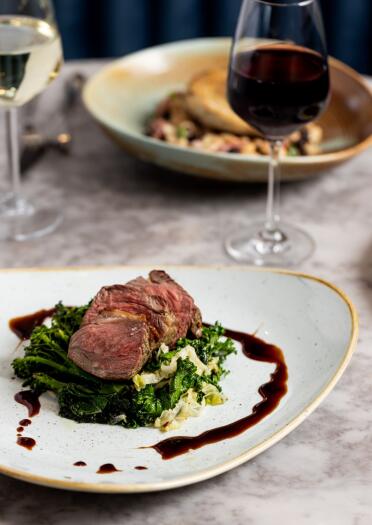 Lamb dish with jus and vegetables and a glass of red wine