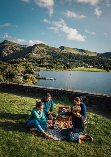 adults ahving a picnic in fromnt of teh lake and mountains of Eryri (Snowdonia)