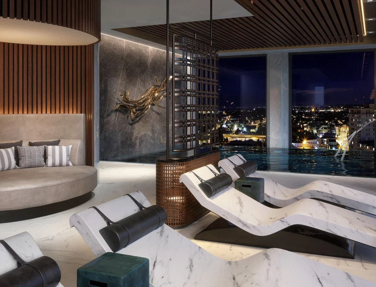Spa beds and loungers by a pool with views of the city beyond.