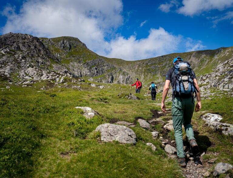 Climbers walking on a path towards a rocky mountain flecked with green.
