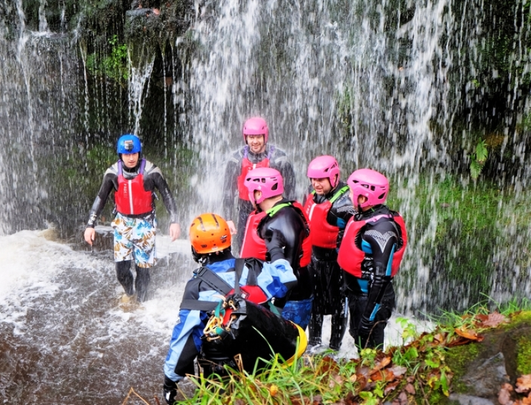 A group of people under a waterfall wearing safety gear.